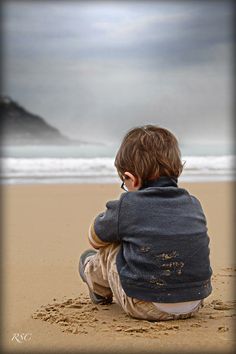 a little boy sitting on top of a sandy beach next to the ocean with a quote above it