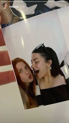 a person holding up a polaroid photo with their face close to another woman's mouth