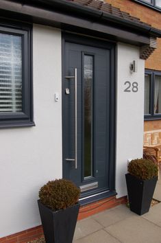 two black planters are next to the front door of a white house with gray trim