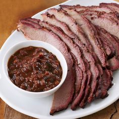 sliced meat and beans on a white plate with a small bowl of sauce next to it