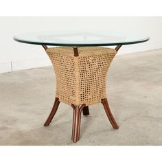 a wicker and glass dining table with wooden legs, on concrete floored area