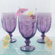 three purple wine glasses with umbrellas on the top and one is filled with ice