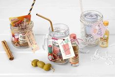 jars filled with different types of items on a white counter top next to cinnamon sticks and olives