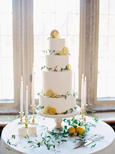 a white wedding cake with lemons and greenery on the top is surrounded by candles