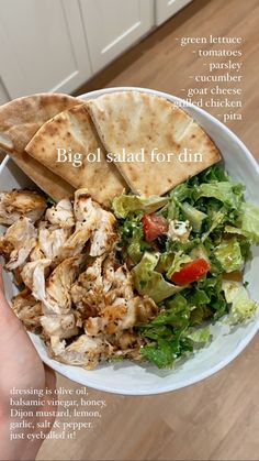 a hand holding a white plate with chicken and salad on it next to pita bread