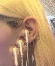 a woman with long blonde hair is wearing ear piercings and holding two white wires