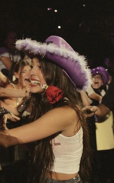 a woman wearing a purple hat and red flower in her hair with other people behind her