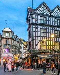 people are walking around in an old european town at dusk, with shops and restaurants lining the street