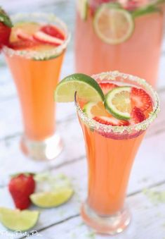 two glasses filled with drinks and garnished with limes, strawberries and lime slices