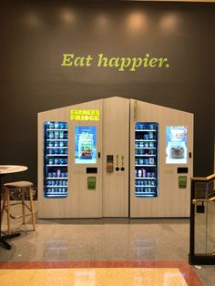 two vending machines in front of a wall that says eat happier with neon lights