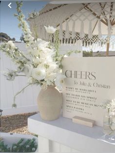 white flowers are in a vase next to a sign that says cheers on the side