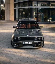 a black car parked in front of a building on a brick road next to tall buildings