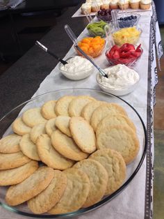 an assortment of cookies on a table with bowls of fruit and dips in the background