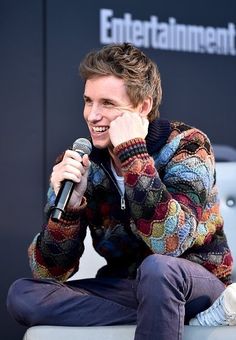 a man sitting on top of a white couch holding a microphone in his hand and smiling