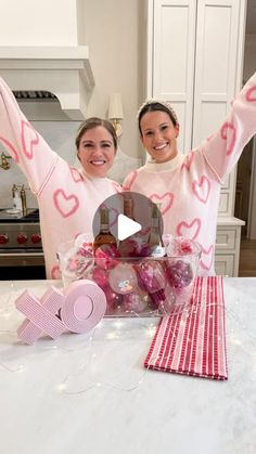 two women in pink sweaters holding up their arms