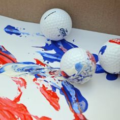 three golf balls sitting on top of a table covered in red, white and blue paint