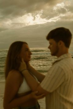 a man standing next to a woman on top of a beach under a cloudy sky