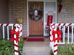 two red and white striped bows are on the front porch of a house decorated for christmas