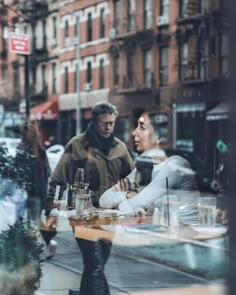 two people sitting at a table in front of a store window looking into the street