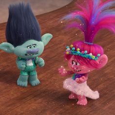 two cartoon characters standing next to each other on a wooden surface with pink and blue hair