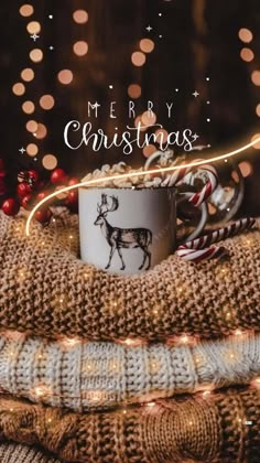 a coffee mug sitting on top of a pile of sweaters with christmas lights in the background