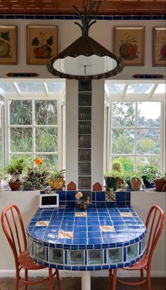 a kitchen table with blue tiles on the top and red chairs around it in front of two windows