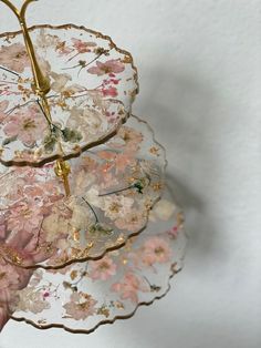 a pink and white flowered plate with gold trimmings is held up by a person's hand