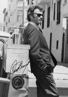 a man in a suit and sunglasses standing next to a box on the street with his hand on his hip