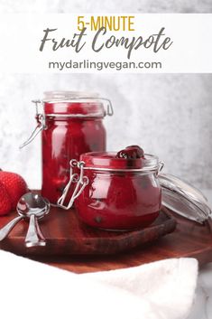 three jars of fruit compote sitting on top of a wooden cutting board next to strawberries