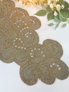 gold beaded coasters with white pearls on them next to flowers and greenery