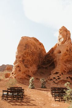 an outdoor ceremony set up in the desert with wooden chairs and flowers on them, surrounded by large rock formations