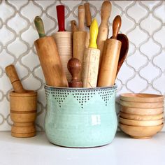 several wooden utensils in a blue bowl on a white counter top next to bowls and spoons