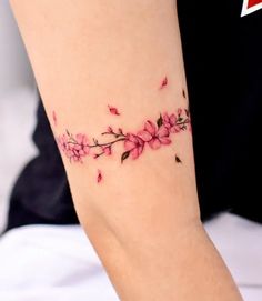 a woman's arm with pink flowers and leaves tattoo on it, sitting on a bed