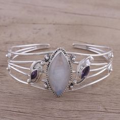 Full of feminine energy, a cabochon of natural rainbow moonstone is flanked by two amethyst gems that total over one carat. This glowing cuff bracelet is designed by Indian artisan Babun Dey. He crafts it with sterling silver wire that circles the wrist. materials: 925 sterling silver, rainbow moonstone, amethyst Combination finish Color(s) may vary slightly Bracelet: 6.25 in. L (end to end) x 1.2 in. W; Pendant(s): 1.2 in. L x 1.4 in. W x 0.4 in. D Amethyst Bangle, Boho Bangle, Amethyst Gem, Adjustable Bangle, Natural Rainbow, Sterling Silver Bangles, Charm Bangle, Handcrafted Earrings, Sterling Silver Necklace Pendants