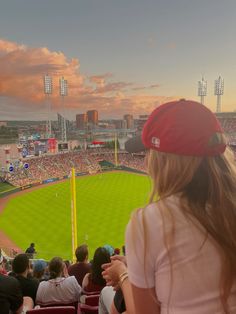 a woman in a red hat is watching a baseball game from the bleachers