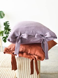 three pillows stacked on top of each other in front of a potted plant and chair