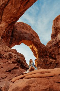 a woman sitting on top of a rock formation with an arch in the back ground