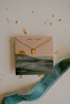 a card with a necklace on it sitting next to a blue ribbon and gold confetti