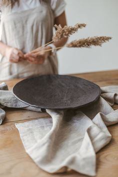 a woman standing over a wooden table with a plate on it and some dried plants in front of her