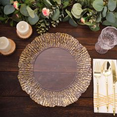 a place setting on a wooden table with candles, napkins and gold plateware