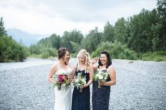 three bridesmaids standing in front of a river with their bouquets on the shore