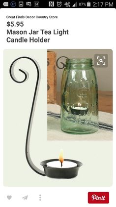 a glass jar with a candle in it sitting on a table next to a metal hook