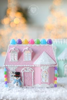 there is a pink toy house with candy on the roof and a snowman in front