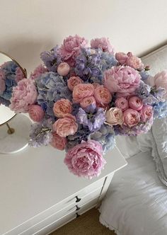 a bouquet of pink and blue flowers sitting on top of a table next to a mirror