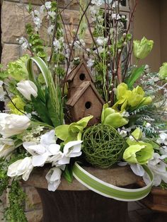 an arrangement of flowers and birdhouse in a vase with ribbon around the base,