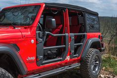 a red jeep is parked on the side of a hill with trees in the background