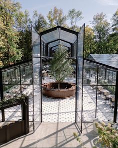 the inside of a glass walled building with tables and chairs around it, surrounded by trees