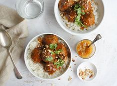 two bowls filled with meat and rice on top of a white table next to a glass of water