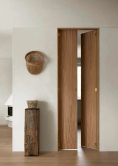 an open door in a white room with wood flooring and a basket hanging on the wall