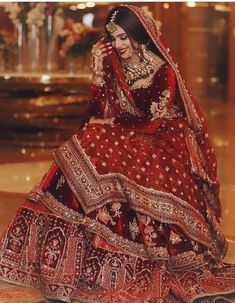 a woman in a red and gold bridal gown sitting on the floor with her hands behind her head